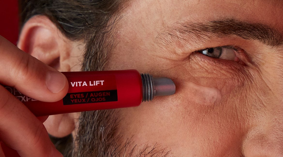 Ein junger Mann trägt Vita Lift Augenpflege von L'Oréal Paris Men Expert auf seine rechte Wange auf